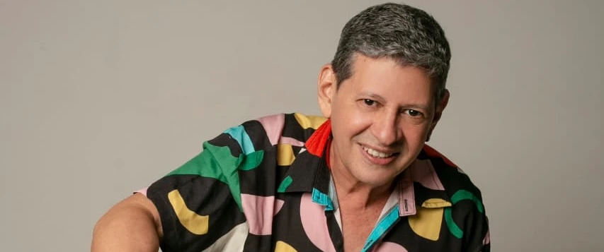 O cantor aparece sorrindo com uma camisa colorida.