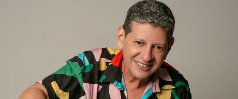 O cantor aparece sorrindo com uma camisa colorida.