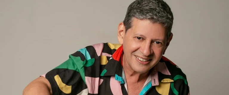 O cantor aparece sorrindo com uma camisa colorida.